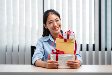 Happy woman is smiling and holding present box with red ribbon in the hands while preparing gift for celebrate