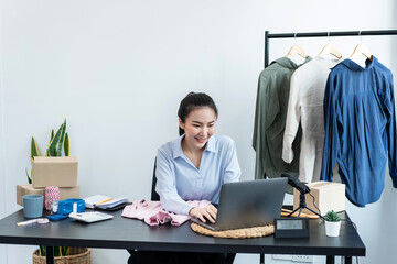 Female fashion designer is checking order customer on laptop and preparing packing clothes in cardboard boxes