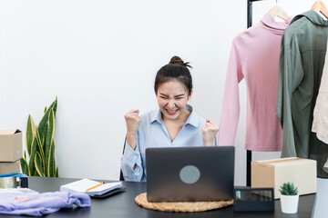 Female fashion designer is celebrating success with arms up after checking order customer on laptop and preparing