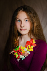 Fototapeta premium A girl in a dress with long hair sits on a chair, wearing a handmade autumn necklace