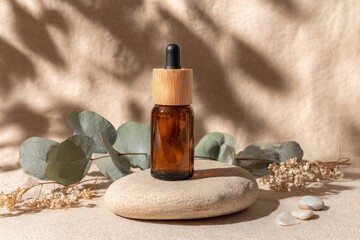 Amber glass bottle with dropper on stone with foliage & shadows, neutral background