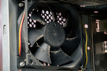 Close-up of a dusty computer case cooling fan inside an old PC, dirty hardware with dust buildup on blades, concept of computer maintenance and overheating problem
