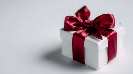 Fototapeta premium A white gift box tied with a rich red satin ribbon and bow set against a clean softly lit background with subtle shadows