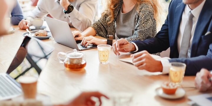 Group of business people in casual meeting, using laptops and taking notes. Business attire, diverse team, collaborative workspace, discussion and teamwork. Business people working together at cafe - Powered by Adobe
