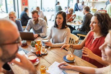 Group of diverse people in a cafe, smiling and talking. Coffee cups and pastries on the table. Casual meeting in a lively cafe setting. Casual startup business team working at a cafe.