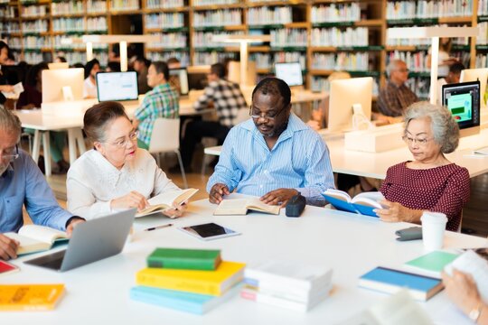 Diverse group reading in library. Men and women, various ethnicities, engaged in books. Library setting, diverse readers, focused on reading and learning. Senior people learning new skills at library.