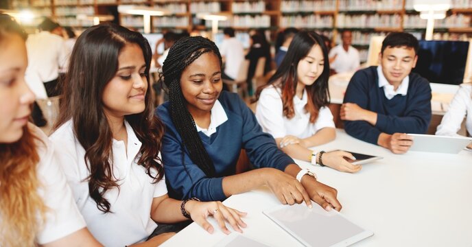 Diverse students studying together in a library, using tablets. Diverse students engaged in learning in library. Diverse students learning together as a group in library. Learning class. Education