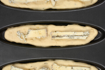 A close-up, overhead shot highlights three portions of unbaked dough with thick pieces of gorgonzola cheese in a non-stick baking pan