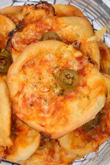 A close-up, appetizing shot of a glass bowl filled with freshly baked mini cheese pizzas, topped with melted golden cheese, herbs, and sliced green olives