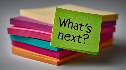 Stacked assortment of colorful sticky notes, with one vibrant green note prominently displaying the question "What's next?" in a  perspective, suggesting brainstorming and future planning amidst...