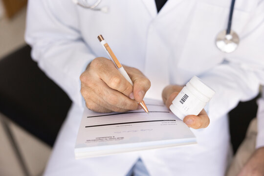 Close up doctor holding medications bottle, writing on prescription pad