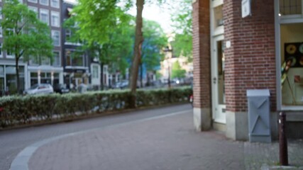 Blurry cyclist rides through a european city street with brick buildings, showcasing defocused urban architecture and greenery, creating a serene outdoor bokeh scene. - Powered by Adobe