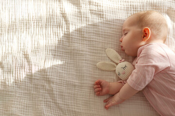 Adorable baby in pink pajamas sleeping peacefully with her toy. Copy space, background.