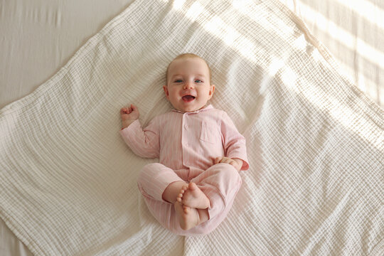 Top view shot of a joyful baby wearing pink pajamas lying on the back and laughing. Copy space, background.