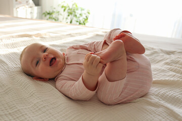 Adorable baby wearing pink pajamas lying on the back and playing with her feet. Copy space, background.