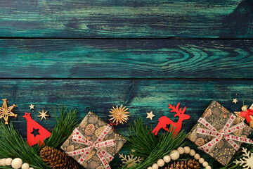 Christmas flat lay with pinecone gifts, straw stars decorations, red cutouts, and pine branches on teal wood background.
