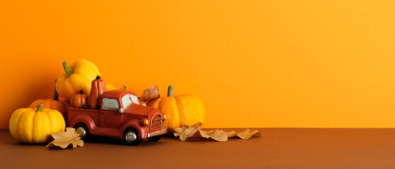 Vintage red truck carries mini pumpkins amid autumn leaves. Fall banner design.