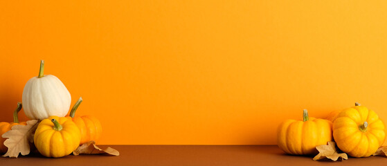 Pumpkins and dry leaves on brown surface with orange backdrop. Autumn, fall, Thanksgiving banner design