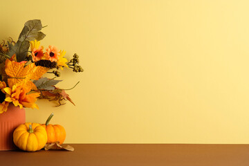 Fall-themed vase with pumpkins and foliage on yellow backdrop. Soft seasonal tones ideal for cozy autumn or Thanksgiving visuals.