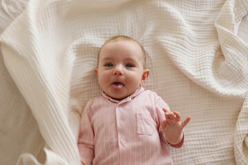 Top view shot of a joyful baby wearing pink pajamas lying on the back and laughing. Copy space, background.