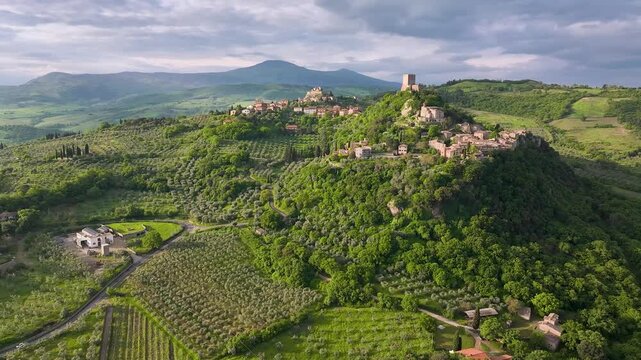 Aerial view of the Rocca d'Orcia and surrounding green hillsides, a landscape of warm, earthy tones contrasting with vibrant green vegetation, Bagno Vignoni, Tuscany, Italy.