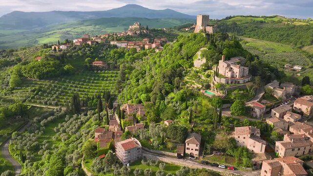 Aerial view of the Rocca di Tentennano, a medieval castle perched atop a lush green hill contrasting with the distant town, Bagno Vignoni, Tuscany, Italy.