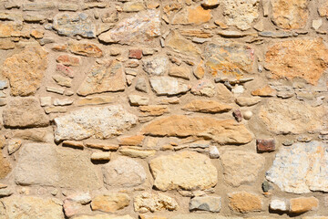 A close-up horizontal shot of an ancient stone wall featuring a mix of irregularly shaped beige and yellow stones bound by thick, rough mortar