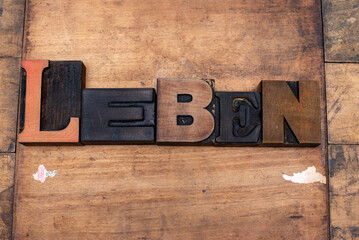 Das Wort Leben mit alten gebrauchten Lettern aus Holz ausgelegt. Der Untergrund besteht aus Altholz. Starke Gebrauchsspuren sind zu erkennen.
