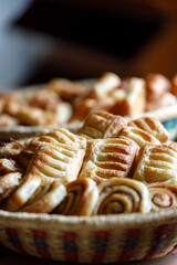 A woven basket filled with assorted golden pastries and bread rolls, freshly baked and served at a rustic wedding breakfast buffet.