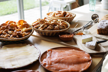 A bright breakfast buffet table with baskets of pastries, sliced cheese, smoked salmon, jams, and soft cheeses for a wedding event.