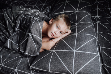 A handsome blond boy is lying in bed