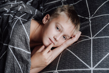 A handsome blond boy is lying in bed