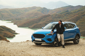 A photo showcasing the blue colored SUV, captured from a front angle emphasizing its left side, with Bovilla Lake in the background, accompanied by a man in a black jacket posing beside it