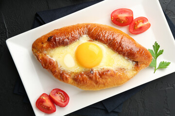 Tasty khachapuri with cheese, egg, tomatoes and parsley on black table, top view