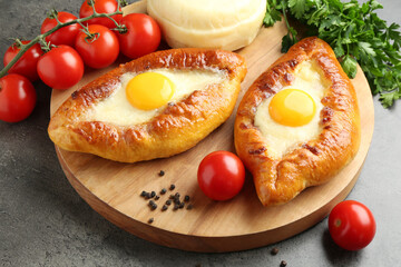 Tasty khachapuris with cheese, eggs, tomatoes and spices on grey textured table