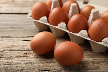 Raw chicken eggs in egg carton on wooden table, closeup