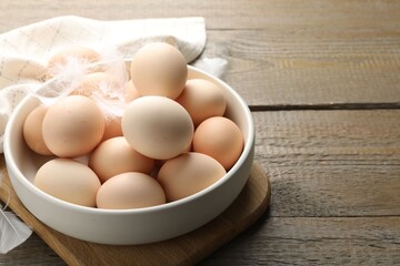 Raw chicken eggs and feathers on wooden table, closeup. Space for text