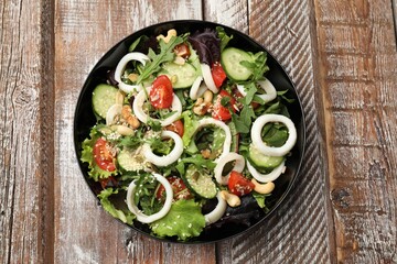 Delicious salad with squid rings, vegetables and nuts on wooden table, top view