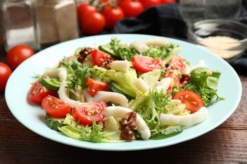 Delicious salad with squid, vegetables and walnuts on wooden table, closeup