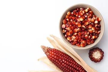 Ripe red corn kernels in bowl and cob on white table, flat lay. Space for text