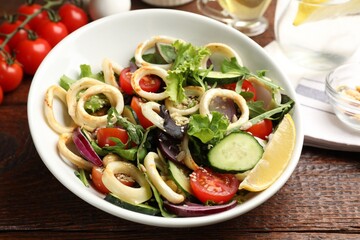 Delicious salad with squid rings and vegetables served on wooden table, closeup