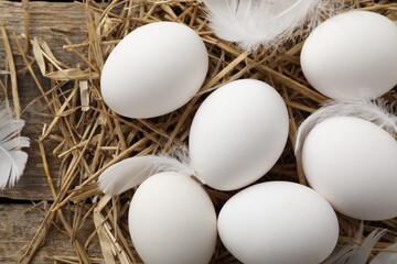 Raw chicken eggs, feathers and straw on wooden table, flat lay