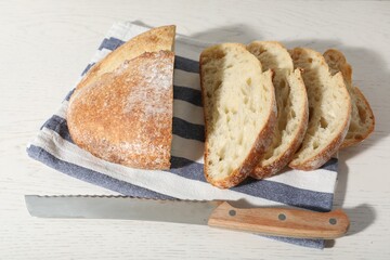 Loaf of fresh bread and knife on white wooden table, above view