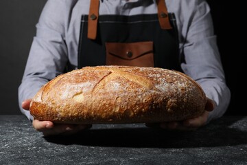 Baker with loaf of fresh bread at grey textured table, closeup