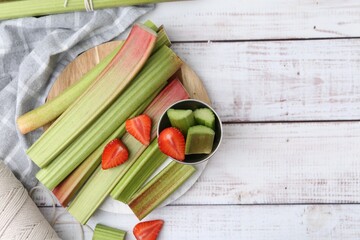 Rhubarb stalks and strawberries on white wooden table, flat lay. Space for text