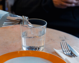 Close-up of a woman's hand pouring water from a glass bottle. Focus on hydration, health, and sustainability in dining/lifestyle