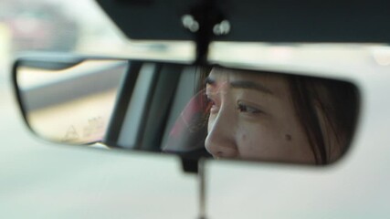 A woman is looking at her reflection in a car's rearview mirror