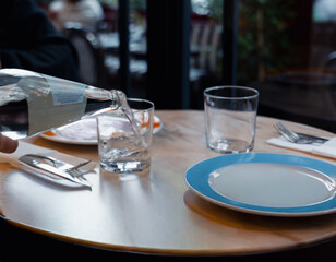 Close-up of a woman's hand pouring water from a glass bottle. Focus on hydration, health, and sustainability in dining lifestyle