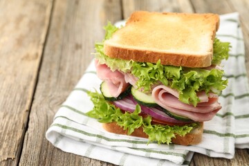 Tasty sandwich with ham and vegetables on wooden table, closeup. Space for text