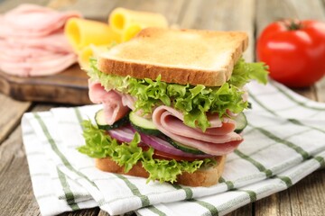 Tasty sandwich with ham and vegetables on wooden table, closeup